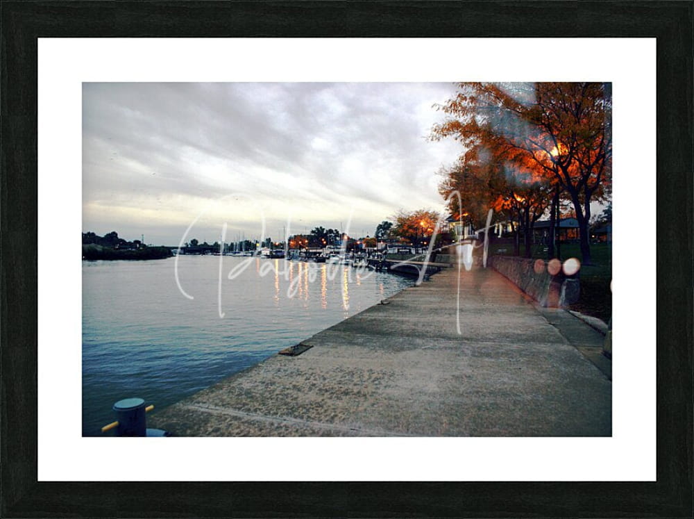 Black-framed art print of dawn on the huron river showing a serene waterfront with autumn trees and boats under clouds