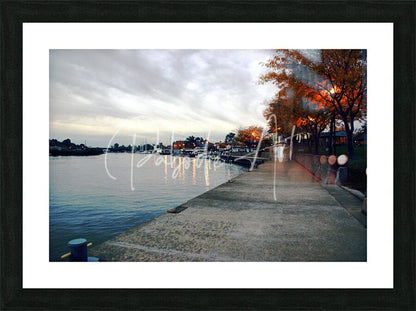 Black-framed art print of dawn on the huron river showing a serene waterfront with autumn trees and boats under clouds