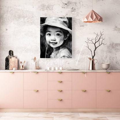 Framed black-and-white portrait artwork of a smiling child wearing a wide-brimmed hat titled kimmie displayed on wall