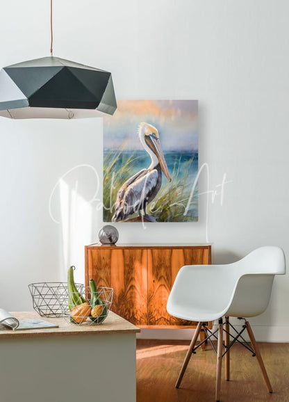 A framed watercolor painting titled Pelican Shores showing a pelican in soft hues standing among tall grass by the ocean