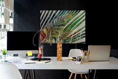 A vibrant tropical palms i leaf painting with bold green teal and white stripes hanging above a modern desk setup