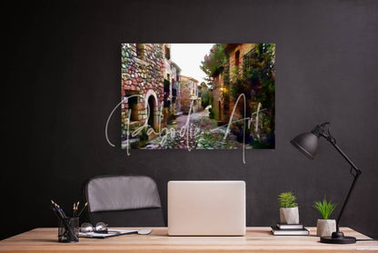 A rectangular framed print of a tuscany cobblestone street with stone buildings and greenery in natural tones